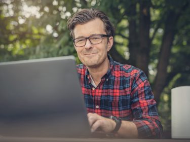 Ein Mann surft mit seinem Laptop, während er unter einem Baum sitzt