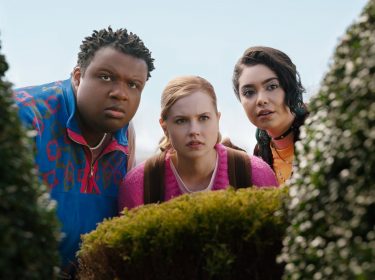 Cady, Janis und Damian schauen von einem Gebüsch aus in die Kamera