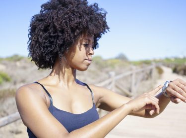 Junge Frau im Freien guckt auf ihre Smartwatch am Handgelenk