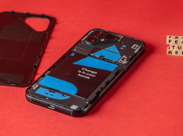 Das schwarze Fairphone 5 liegt mit abgetrennter Rückseite auf einem roten Untergrund, im Hintergrund ergeben Buchstabenwürfel den Schriftzug featured