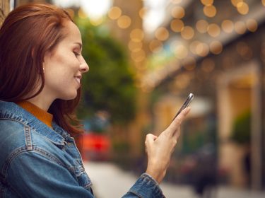 Eine junge Frau schaut auf ihr Handy und lächelt dabei.
