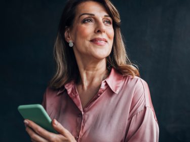 Eine Frau hält ihr Smartphone in der Hand und lächelt