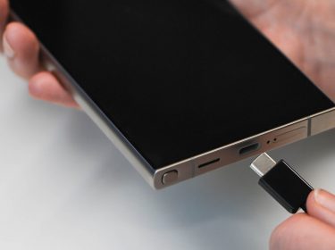 rechte Hand hält ein Galaxy S24 Ultra vor einem weißen Hintergrund, die linke Hand hält ein USB-Kabel