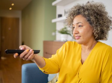 Frau sitzt auf dem Sofa und drückt auf ihre Fernbedienung