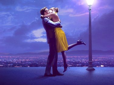Auf dem Bild zu GigaTV-Filme an Valentinstag sind Emma Stone und Ryan Gosling in einer romantischen Szene aus dem Film La La Land zu sehen. Die beiden umarmen und küssen sich leidenschaftlich unter einer leuchtenden Straßenlaterne mit Blick auf die funkelnde Skyline von Los Angeles. Emma Stone trägt ein auffälliges gelbes Kleid und schwarze High Heels, während Ryan Gosling einen dunklen Anzug trägt. Die Szene strahlt eine verträumte und magische Atmosphäre aus, perfekt für einen romantischen Filmabend.