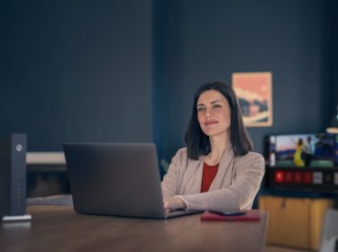 Frau sitzt mit Laptop neben Kabel Router