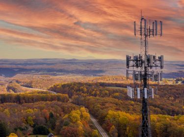 Ein Sendemast in einer ländlichen Gegend, in der eine Straße durch einen Wald führt.
