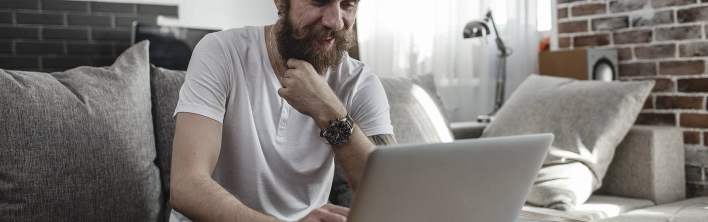 Ein Mann sitzt auf der Couch und nutzt dabei einen Laptop auf dem Tisch vor sich.