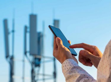 Eine Person mit einem Smartphone in der Hand während sich im Hintergrund ein Telekommunikationsturm befindet