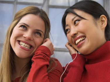 Zwei Frauen, die sich kabelgebundene Kopfhörer teilen.