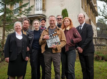 Schauspieler posieren vor DRehbeginn vor einem Haus.