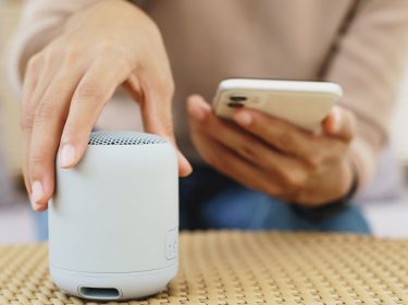 Nahaufnahme von einer Hand, die einen Lautsprecher mit einem Smartphone verbinden will.