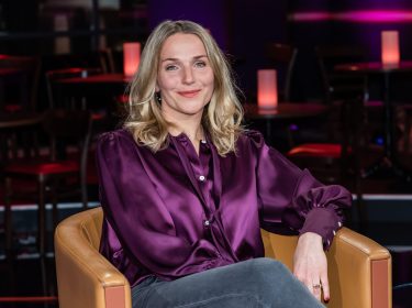 Schauspielerin Tanja Wedhorn sitzt mit lila Bluse auf dem Stuhl eines Fernsehstudios