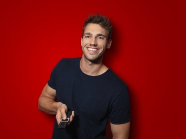 Ein Mann hält eine Tv-Fernbedienung in der Hand und lächelt