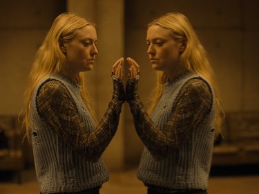 Die Hauptfigur Mina steht an der Glasscheibe des Bunkers