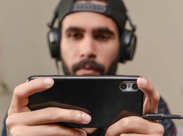 Ein Mann hat ein Headset auf seinem Kopf und spielt auf seinem Smartphone Mobile Games