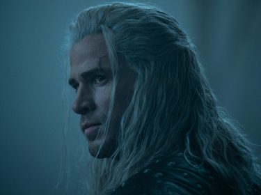 Auf dem Bild zu The Witcher Staffel 4 ist Liam Hemsworth als Geralt von Riva zu sehen. Er trägt langes, silbernes Haar, eine Narbe über dem Auge und eine schwarze Lederrüstung mit Nieten.