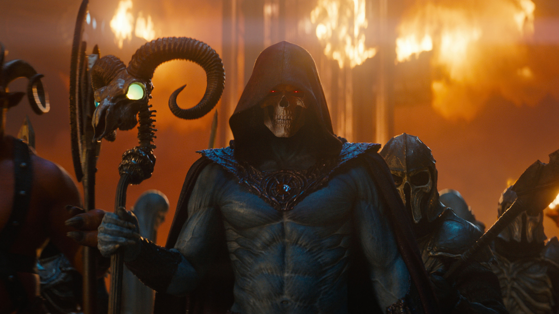 Im Bild zum Masters of the Universe neuer Film ist Skeletor, gespielt von Jared Leto, in bedrohlicher Pose zu sehen. Mit leuchtend roten Augen, Kapuze und Totenschädel-Gesicht hält er einen Stab mit leuchtendem Kristall. Hinter ihm lodern Flammen, umgeben von dunklen Kriegern – die Szene wirkt düster, mächtig und apokalyptisch.