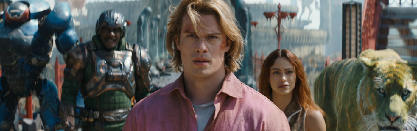 Im Bild zum Masters of the Universe neuer Film ist Adam, gespielt von Nicholas Galitzine, im Vordergrund mit entschlossenem Blick zu sehen. Hinter ihm stehen Teela (Camila Mendes), Man-At-Arms (Idris Elba), Roboto (Kristen Wiig) und der grüne Tiger Cringer. Die Szene wirkt episch und angespannt, mit einer fantasievollen, mittelalterlich-futuristischen Kulisse im Hintergrund.