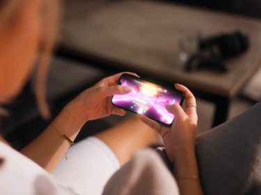 Eine Frau hält ein Handy in der Hand und spielt darauf ein Rennspiel.