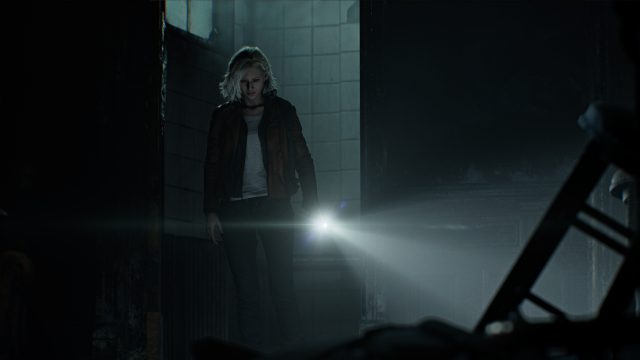 In dieser Szene aus Resident Evil Requiem betritt Protagonistin Grace Ashcroft einen düsteren, verfallenen Raum. Mit ernster Miene leuchtet sie mit einer Taschenlampe in die Dunkelheit. Die Umgebung wirkt verlassen und bedrohlich – schmutzige Kacheln, kaputte Möbel und schwaches Licht unterstreichen die unheimliche Atmosphäre von Resident Evil 9