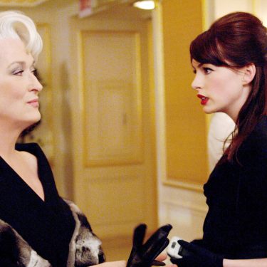 Auf dem Bild zum möglichen Film Der Teufel trägt Prada 2 sind Meryl Streep als Miranda Priestly und Anne Hathaway als Andy Sachs zu sehen. In einer eleganten Umgebung stehen sich die beiden Charaktere gegenüber. Miranda blickt kühl und überlegen, während Andy ernsthaft und entschlossen wirkt. Die Szene vermittelt Spannung und Stilbewusstsein.