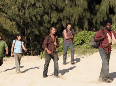 Fünf Überlebende des Flugzeugabsturzes in der Serie Lost kommen gerade aus dem Dschungel an den Strand gewandert. Sie tragen Rucksäcke. Allen voran geht