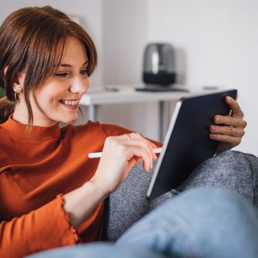 Auf dem Bild im Artikel dazu, wie Du Vodafone digital erreichen kannst, sitzt eine junge Frau entspannt auf einem Sofa und nutzt ein Tablet mit einem Eingabestift.