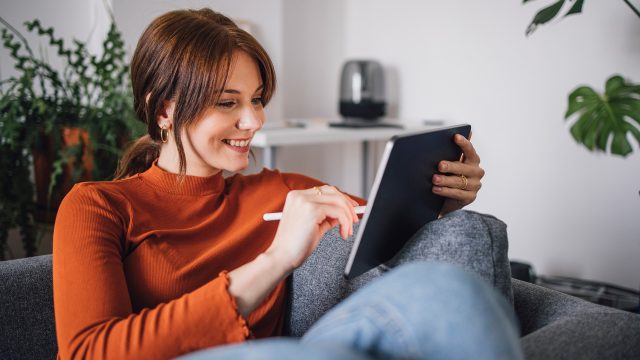 Auf dem Bild im Artikel dazu, wie Du Vodafone digital erreichen kannst, sitzt eine junge Frau entspannt auf einem Sofa und nutzt ein Tablet mit einem Eingabestift.
