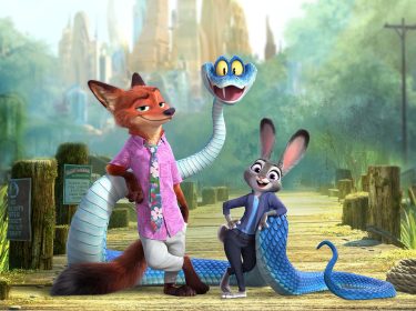 Auf dem Bild zu Zoomania 2 stehen drei tierische Charaktere im Fokus: Ein selbstbewusst wirkender Fuchs in Hawaiihemd, eine fröhlich lächelnde Häsin in Polizeiuniform und eine blaue Schlange mit großen gelben Augen. Die Szenerie spielt auf einem Holzsteg vor grüner Landschaft.