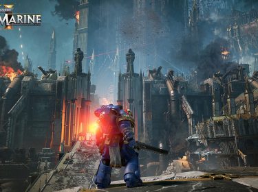 Auf dem Bild aus Warhammer 40.000: Space Marines 2 steht ein einzelner Space Marine in blauer Rüstung mit einer Kettensägewaffe vor einer gewaltigen, gotischen Festung. Flammen und Rauch steigen aus der Festung empor, während Laserstrahlen den Himmel durchschneiden. Die Architektur ist imposant und düster, mit Türmen und riesigen Rohren. Der Space Marine blickt in Richtung des Schlachtfelds, bereit für den Kampf. Das Bild unterstreicht die epische und düstere Stimmung des Spiels.