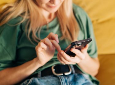 Frau sitzt mit iPhone in der Hand auf dem Sofa
