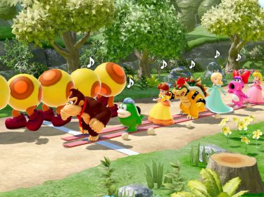Auf diesem Bild aus dem Super Mario Party-Jamboree-Test sieht man eine bunte Reihe von Nintendo-Charakteren, die auf einem Pfad hintereinander marschieren. Angeführt wird die Gruppe von Donkey Kong, gefolgt von Figuren wie Yoshi, Daisy, Bowser, Rosalina, Birdo, Peach und Luigi. Vor Donkey Kong läuft ein großer, gelber Wiggler mit fröhlichem Gesichtsausdruck. Die Umgebung ist eine grüne, lebendige Waldlandschaft mit Blumen und Bäumen, und Musiknoten über den Köpfen der Charaktere zeigen, dass sie im Rhythmus marschieren.