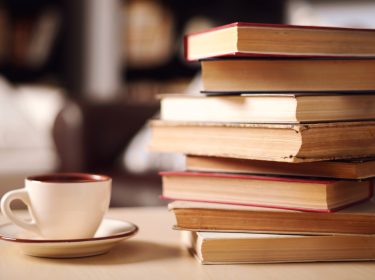 Ein Stapel Bücher liegt auf einem Tisch neben einer Kaffeetasse.