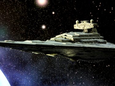 Auf dem Bild in dem Artikel über die neue Star Wars-Trilogie ist ein Raumschiff zu sehen, welches im Weltraum schwebt. Im Hintergrund sieht man die Lichter des Weltalls auf einem dunklen Hintergrund.