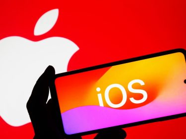 Das Logo von iOS ist auf einem iPhone abgebildet, das von einer menschlichen Hand hochgehalten wird.