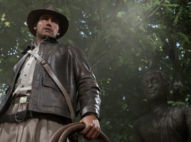Auf dem Bild in dem Artikel zum „Indiana Jones und der große Kreis“-Test ist Indiana Jones in typischer Abenteurerkleidung zu sehen, mit braunem Hut, Lederjacke und einer Peitsche in der Hand. Er steht in einem dichten Dschungel vor einer alten Buddha-Statue, während Sonnenlicht durch die Baumkronen fällt. Die Szene wirkt geheimnisvoll und abenteuerlich.