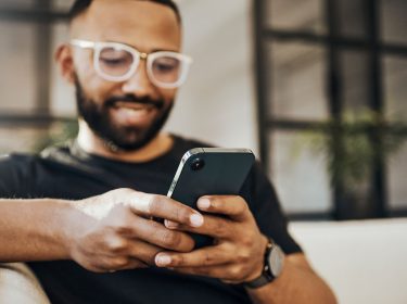 Ein Mann sitzt auf einer Couch und hält ein Handy in der Hand