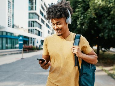Ein junger Mann auf der Straße hat ein Smartphone in der Hand und ein Headset auf dem Kopf.