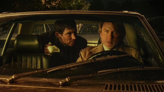 Josh O'Connor und Daniel Craig sitzen in einer Szene von "Wake Up Dead Man: A Knives Out Mystery" nachts in einem Auto.