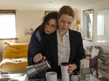 Auf dem Bild aus dem Film Wunderschön mit Karoline Herfurth sind Sonja (Karoline Herfurth) und Vikcy (Nora Tschirner) in einer vertrauten Szene in einer gemütlichen Wohnung zu sehen. Viky lehnt sich mit geschlossenen Augen an Sonjas Schulter, während Sonja konzentriert Kaffee in eine Tasse gießt. Sie trägt einen dunklen Blazer und eine helle Bluse, während Viky lässig gekleidet ist. Die Stimmung ist ruhig und intim.