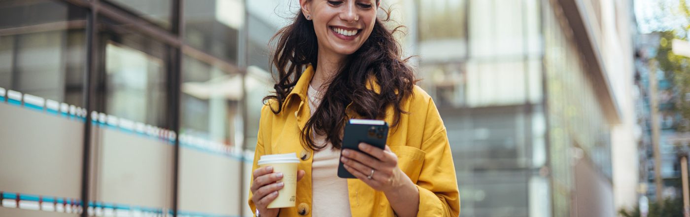 Eine Frau hält einen Kaffee und ein Handy in der Hand
