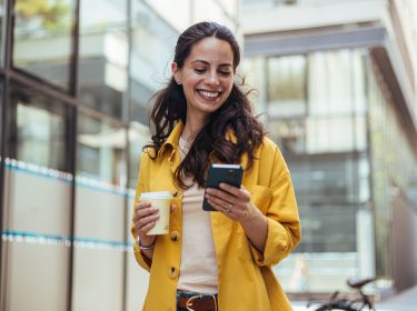 Eine Frau hält einen Kaffee und ein Handy in der Hand