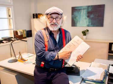 Klaus-Peter Wolf sitzt auf dem Schreibtisch der Hauptkommissarin Ann Kathrin Klaasen aus den Ostfriesenkrimis