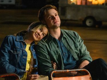 Auf dem Bild aus Bridget Jones 4 sind Bridget Jones, gespielt von Renée Zellweger, und Roxter, dargestellt von Leo Woodall, zu sehen. Bridget lehnt sich entspannt an Roxters Schulter, beide wirken ruhig und zufrieden. Sie sitzen in einer nächtlichen Outdoor-Szene auf einfachen Stühlen, während Bridget eine Bierflasche in der Hand hält. Im Hintergrund ist eine unscharfe Umgebung mit einem Anhänger und warmem Licht zu erkennen.