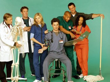 Auf dem Bild zum Scrubs Reboot sind die Hauptcharaktere aus der Serie in einer humorvollen Gruppenaufnahme zu sehen. Von links nach rechts stehen Dr. Bob Kelso (Ken Jenkins) mit einem Skelett, Dr. Cox (John C. McGinley) mit verschränkten Armen, Dr. Elliot Reid (Sarah Chalke) in blauer Kleidung, J.D. (Zach Braff) sitzend mit Stethoskop, Turk (Donald Faison) in grüner Kleidung, der Hausmeister (Neil Flynn) mit einem Wischmopp und Carla (Judy Reyes) in orangefarbener Kleidung. Die Szene ist lebendig und voller Witz.