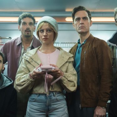 Die Crew von Berlin steht versammelt vor einem Gemälde.