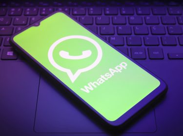 Ein Smartphone, auf dem das Logo von WhatsApp abgebildet ist, liegt auf einer Laptop-Tastatur.