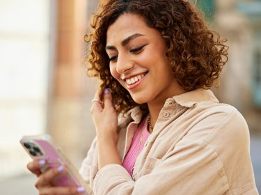 Eine Frau schaut lächelnd auf ein Smartphone.