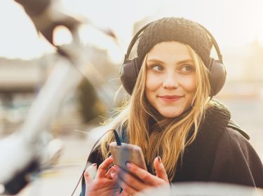 Eine junge Frau hört mit Kopfhörern Musik vom Smartphone.